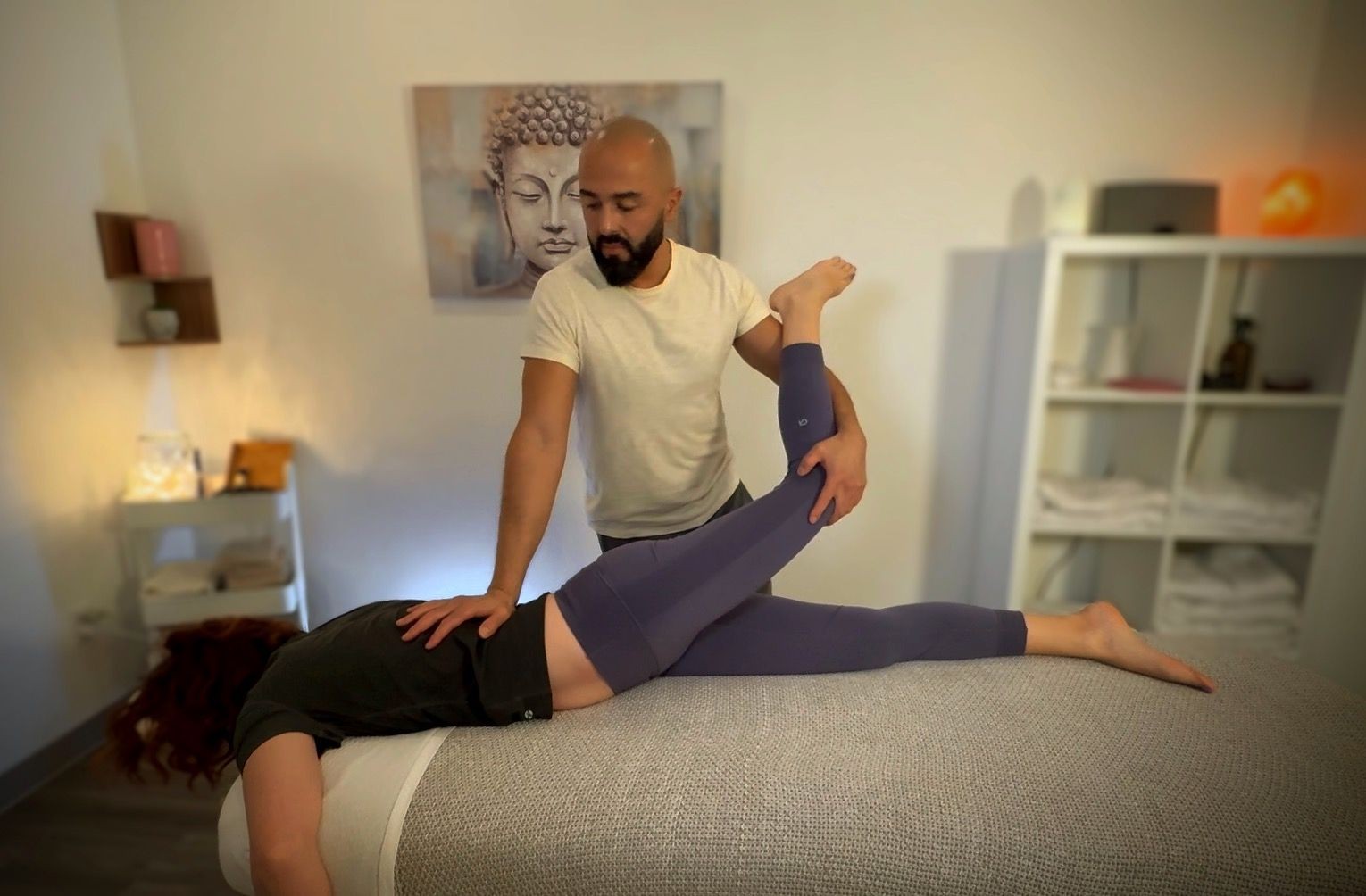 Massage therapist performing stretching exercise on client's leg in a calming room.