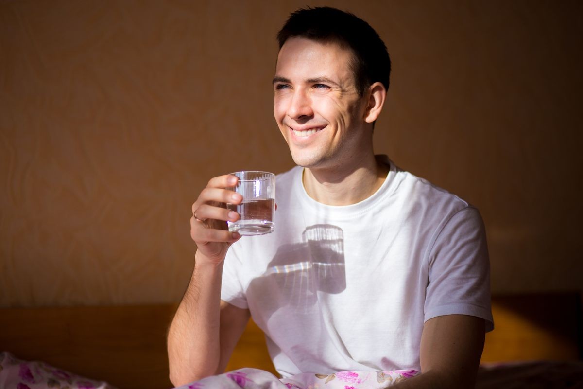 young healthy man stretching after sleep with glass of water, drink every day. Concept of healthy habits